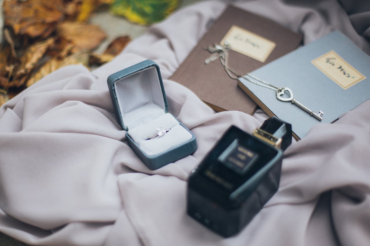 A romantic setup featuring a ring, vintage key, and perfume on soft fabric with autumn leaves.